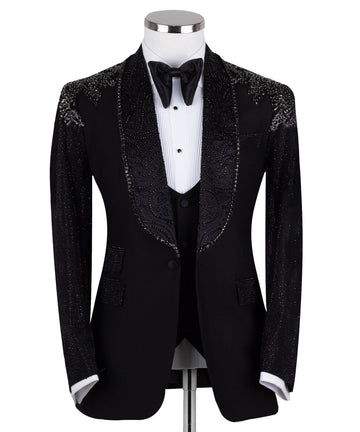 Black three-piece tuxedo on a mannequin, featuring a heavily hand-embellished shawl lapel, shoulders, and sleeves with intricate sparkling beadwork. The tuxedo includes a matching black vest and trousers, designed in a slim fit style, showcasing luxurious craftsmanship from Istanbul.
