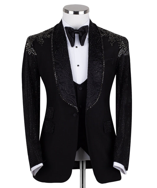 Black three-piece tuxedo on a mannequin, featuring a heavily hand-embellished shawl lapel, shoulders, and sleeves with intricate sparkling beadwork. The tuxedo includes a matching black vest and trousers, designed in a slim fit style, showcasing luxurious craftsmanship from Istanbul.