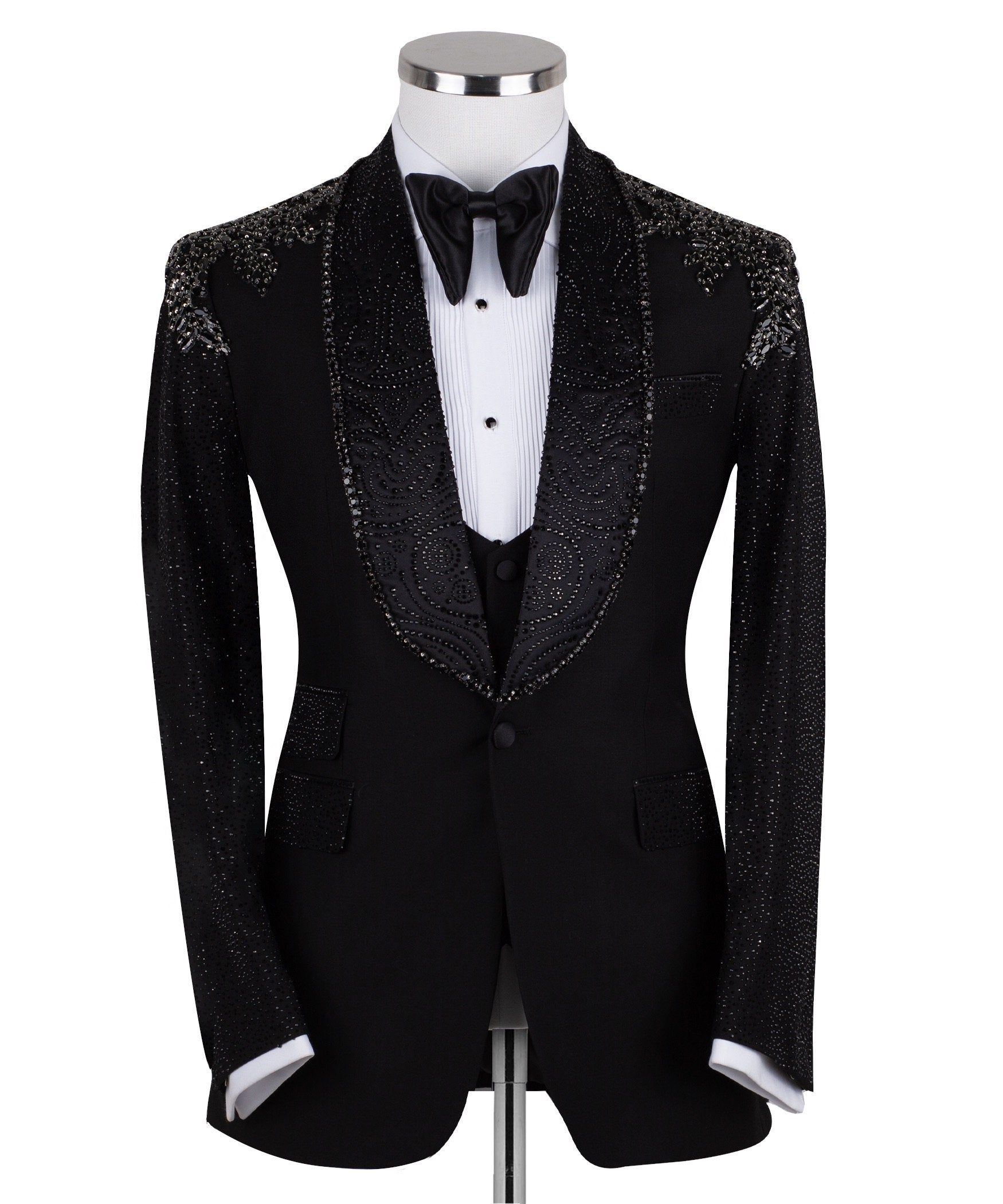 Black three-piece tuxedo on a mannequin, featuring a heavily hand-embellished shawl lapel, shoulders, and sleeves with intricate sparkling beadwork. The tuxedo includes a matching black vest and trousers, designed in a slim fit style, showcasing luxurious craftsmanship from Istanbul.
