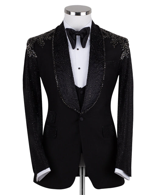 Black three-piece tuxedo on a mannequin, featuring a heavily hand-embellished shawl lapel, shoulders, and sleeves with intricate sparkling beadwork. The tuxedo includes a matching black vest and trousers, designed in a slim fit style, showcasing luxurious craftsmanship from Istanbul.