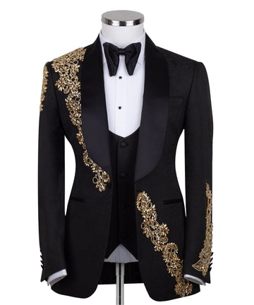 Front view of a black jacquard three-piece tuxedo with intricate gold hand-embellishments on the shawl lapel, shoulder, and cuffs, displayed on a mannequin. From Charly Luxury, handcrafted in Istanbul.