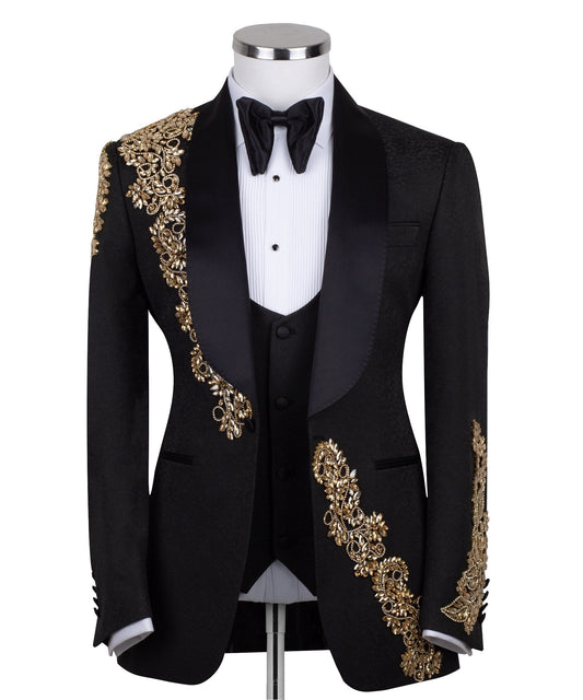 Front view of a black jacquard three-piece tuxedo with intricate gold hand-embellishments on the shawl lapel, shoulder, and cuffs, displayed on a mannequin. From Charly Luxury, handcrafted in Istanbul.