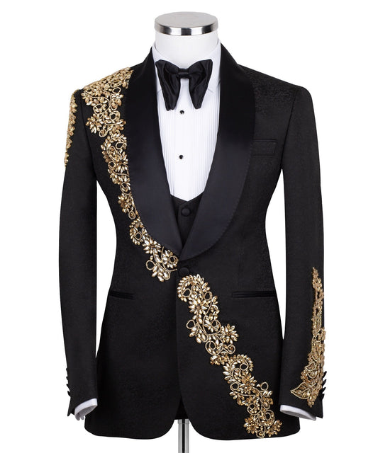 Front view of a black jacquard three-piece tuxedo with intricate gold hand-embellishments on the shawl lapel, shoulder, and cuffs, displayed on a mannequin. From Charly Luxury, handcrafted in Istanbul.