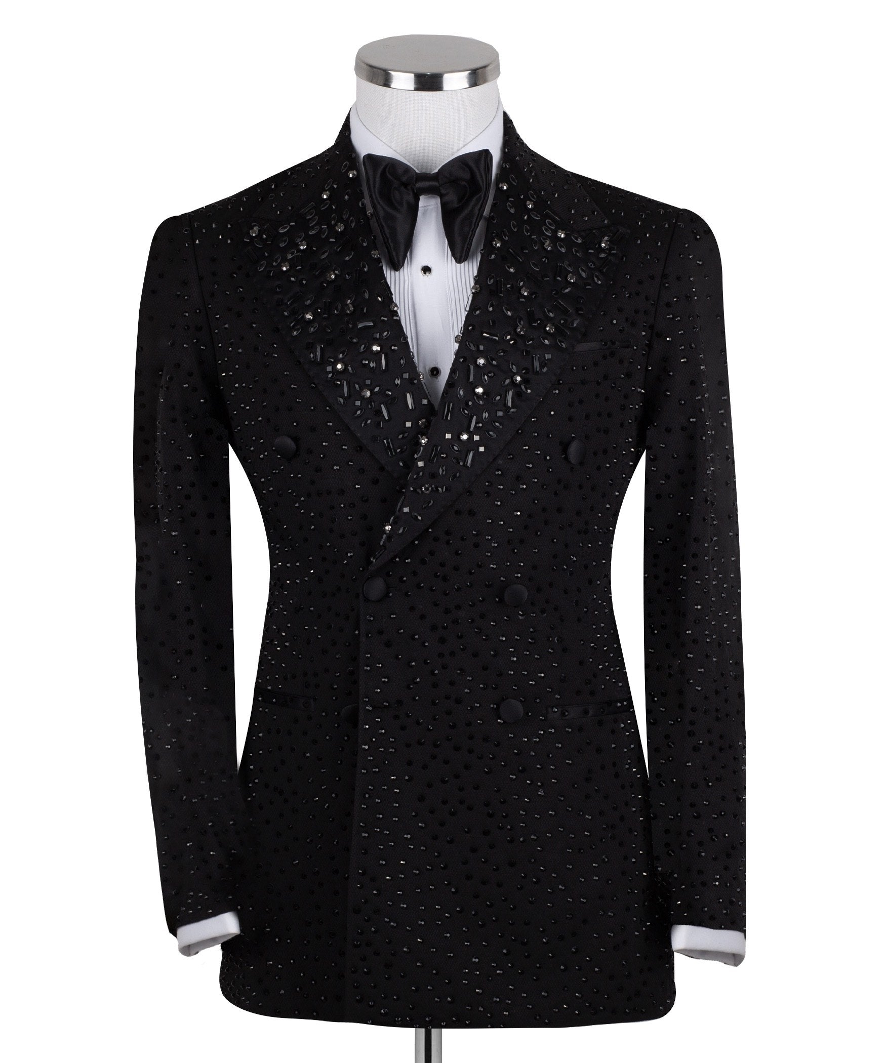 Close-up of a black double-breasted tuxedo jacket on a mannequin, showcasing intricate hand-embellishments with beads and crystals on the lapels and body. Features a peak lapel and black buttons, paired with a white shirt and black bow tie. Front view showing the full jacket and details.