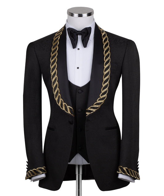Front view of Charly Luxury's black jacquard three-piece tuxedo with opulent gold chain embellishments on the shawl lapel and cuffs, tailored in Istanbul. Includes jacket, vest, and trousers.