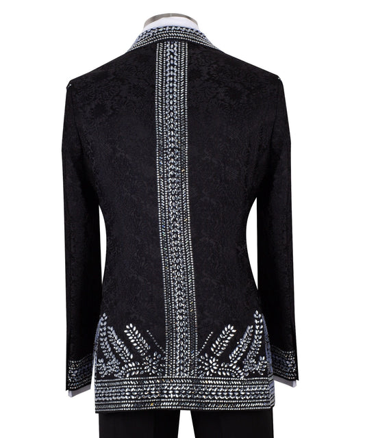 Front view of a black double-breasted tuxedo jacket with extensive silver embellishments, featuring a peak lapel and slim fit design on a mannequin. Back view and close-up showing intricate hand-beading detail.