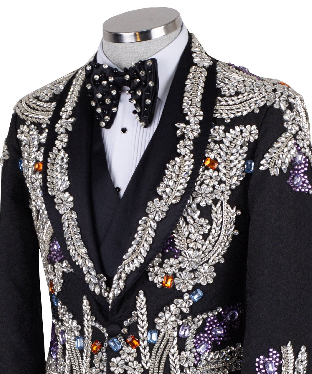 Front and side view of a black tuxedo jacket with extensive silver, purple, orange, and blue crystal and gemstone embellishments in floral and baroque patterns, paired with matching black trousers and vest, on a mannequin. Showcases intricate hand-embellished details and luxurious craftsmanship from Charly Luxury, Istanbul.