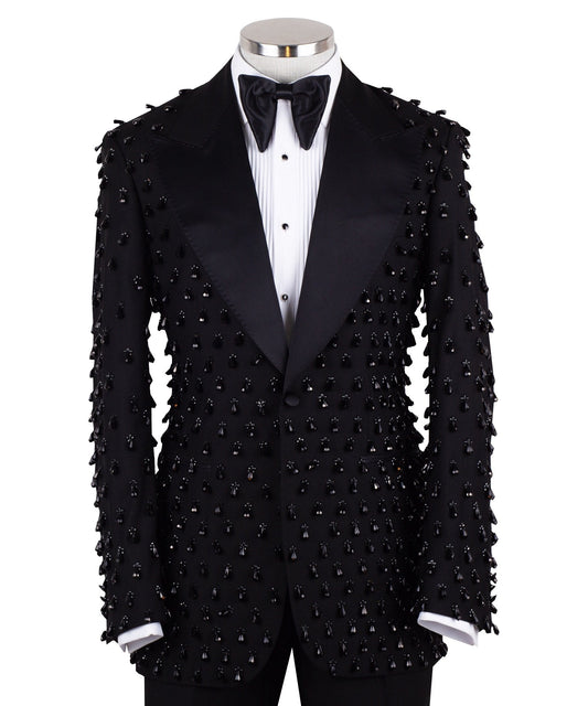 Front view of a black hand-embellished luxury tuxedo jacket with satin peak lapels and matching trousers on a mannequin. Side view close-up of the jacket's intricate black bead embellishments. Close-up of the tuxedo trousers with a satin side stripe and high-waisted detail.