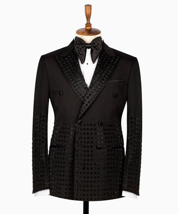 Front view of a black double-breasted tuxedo jacket featuring intricate hand-embellished studs on the peak lapels, shoulders, sleeves, and lower body, styled with matching black trousers with a satin side stripe. Handcrafted luxury from Charly Luxury Istanbul.