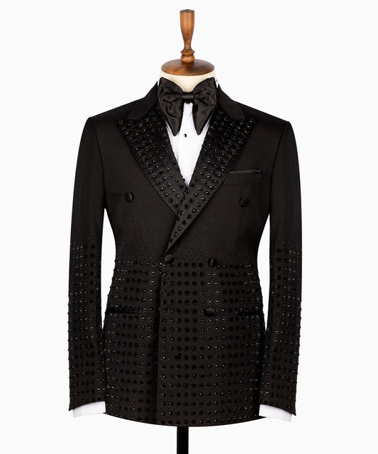 Front view of a black double-breasted tuxedo jacket featuring intricate hand-embellished studs on the peak lapels, shoulders, sleeves, and lower body, styled with matching black trousers with a satin side stripe. Handcrafted luxury from Charly Luxury Istanbul.
