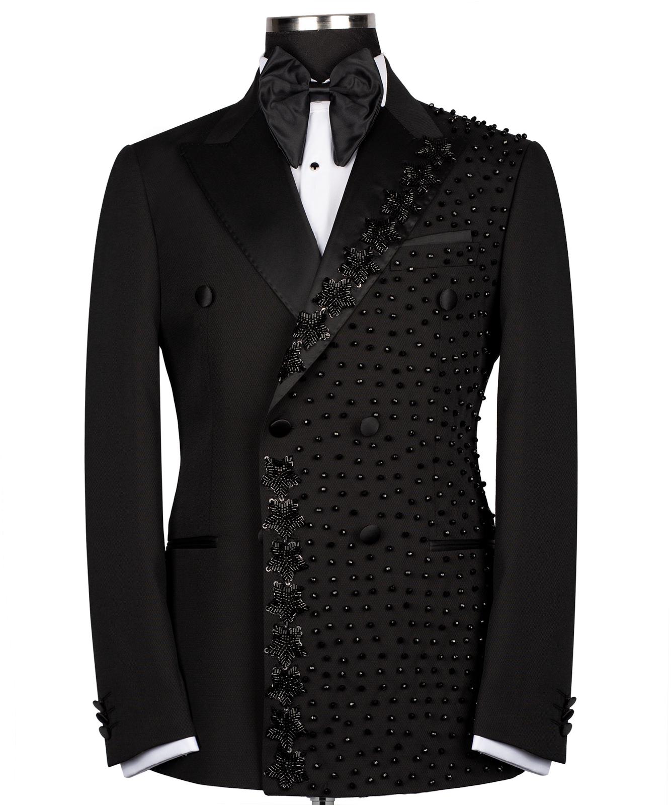 Front view of a black double-breasted tuxedo jacket with satin peak lapels and intricate hand-embellished black beading on the right side. Paired with matching trousers featuring a satin side stripe. High-end bespoke formal wear, handcrafted in Istanbul.