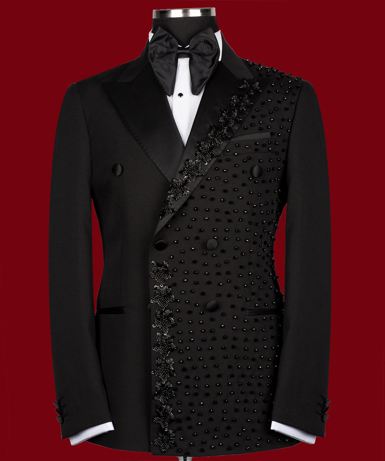 Front view of a black double-breasted tuxedo jacket with satin peak lapels and intricate hand-embellished black beading on the right side. Paired with matching trousers featuring a satin side stripe. High-end bespoke formal wear, handcrafted in Istanbul.
