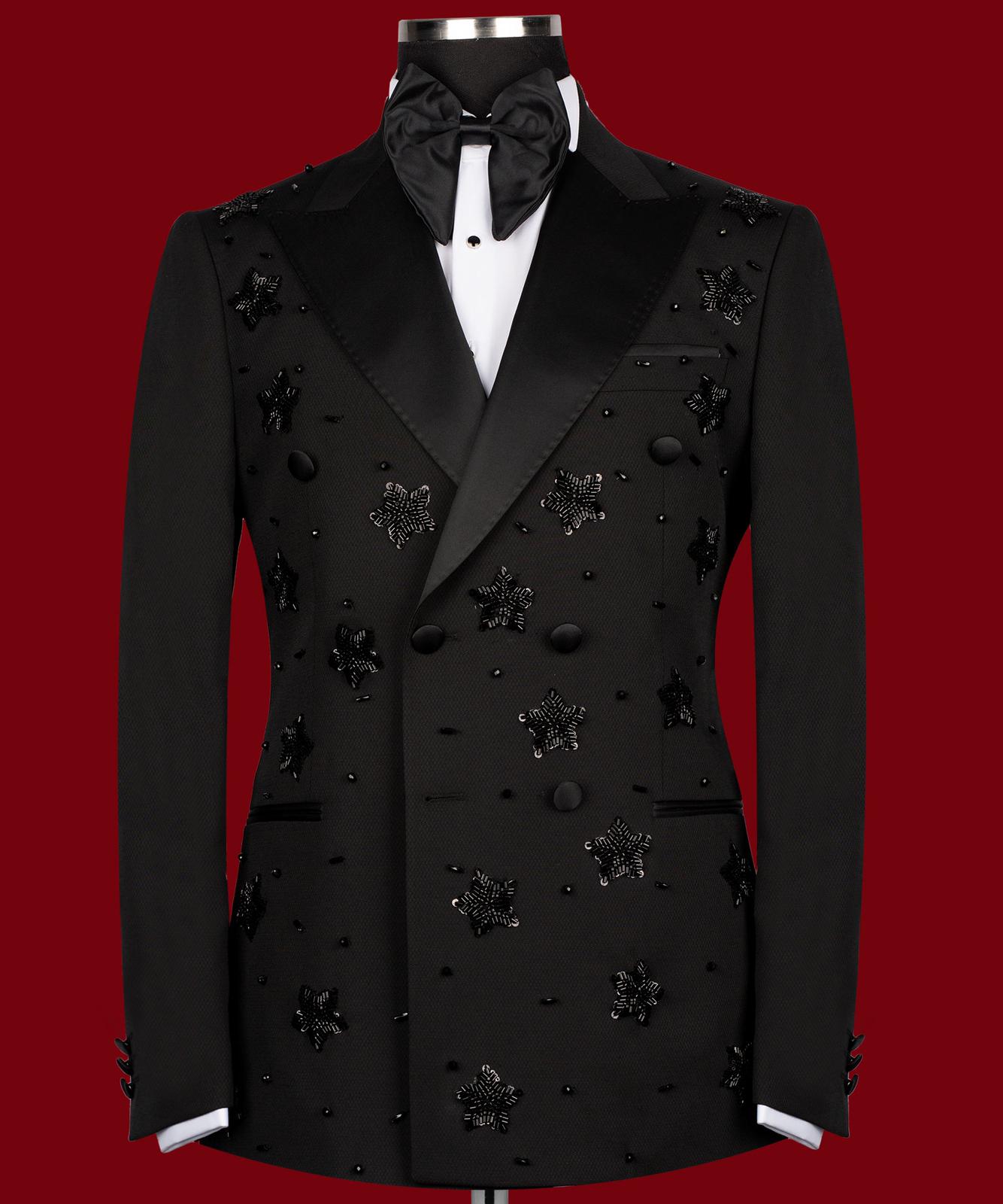 Front view of a black double-breasted tuxedo with satin peak lapels, adorned with intricate black beaded starburst embellishments, worn by a mannequin. The matching trousers with satin side stripe are also shown. This luxurious evening wear is handcrafted in Istanbul by Charly Luxury.