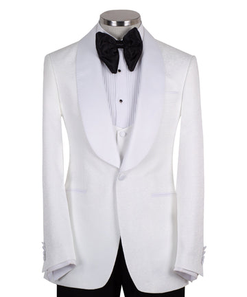 Front view of a white jacquard patterned single-breasted tuxedo jacket with a white satin shawl lapel, displayed on a mannequin. Includes a matching white jacquard vest and black trousers. Handmade in Istanbul luxury bespoke menswear.
